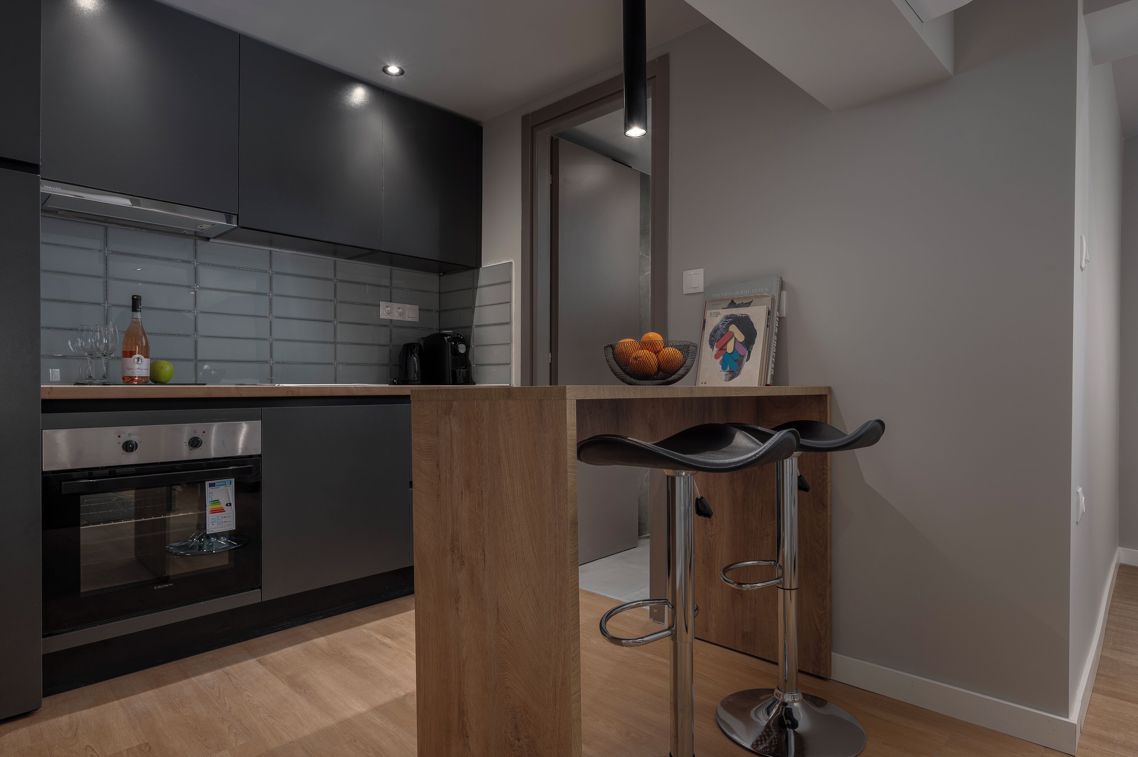 Een moderne keuken met donkere kastjes, een ingebouwde oven en een bar met krukken.