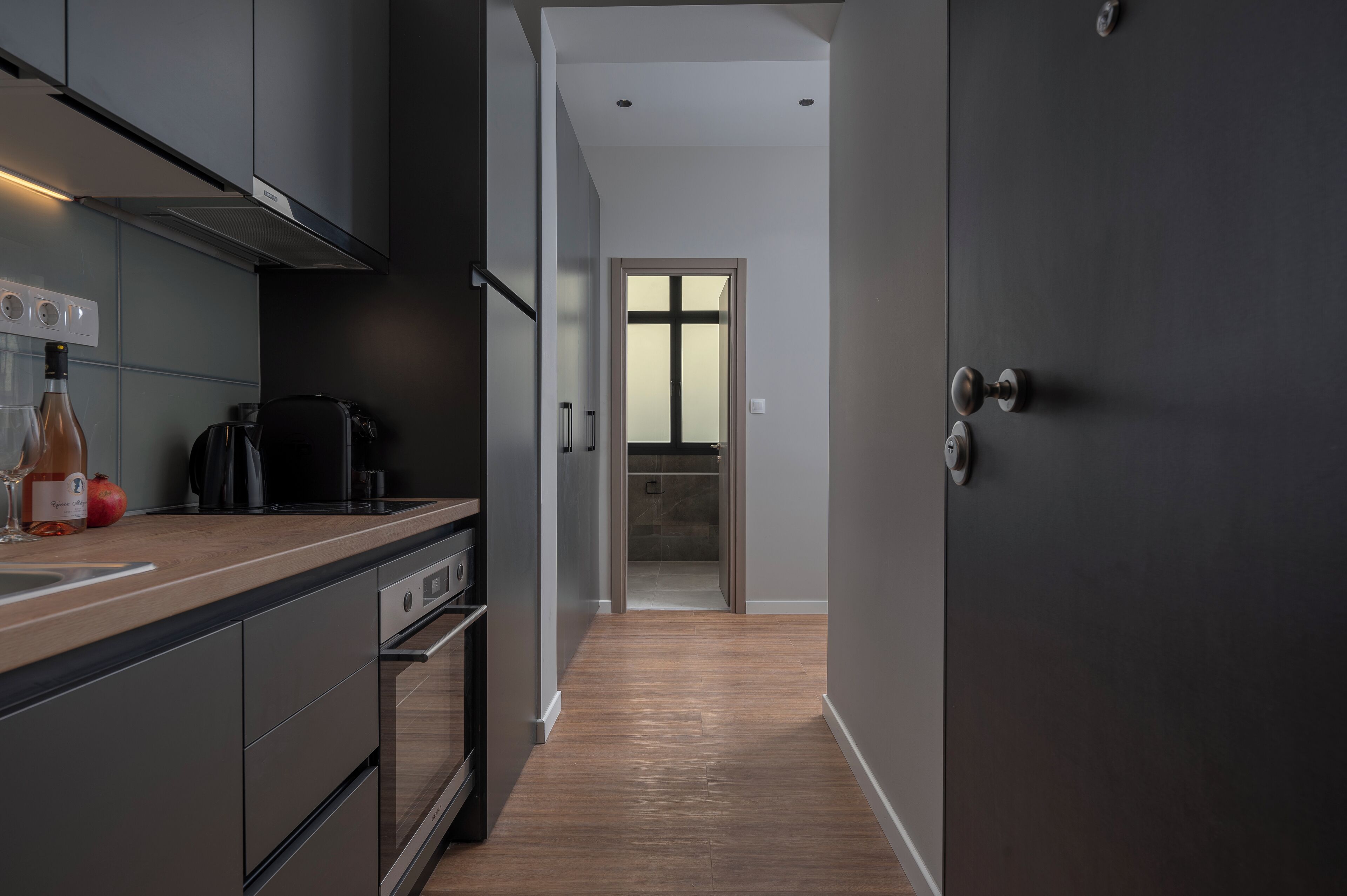 A modern kitchen with stainless steel appliances, a wooden countertop, and a dark door.