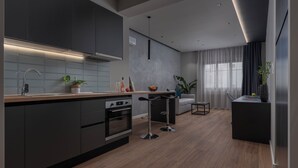 A modern kitchen with dark cabinets, a wooden countertop, and a built-in oven. There are two bar stools and a small table with a vase of flowers. - Hebrard Industrial Suites (Thessaloniki)