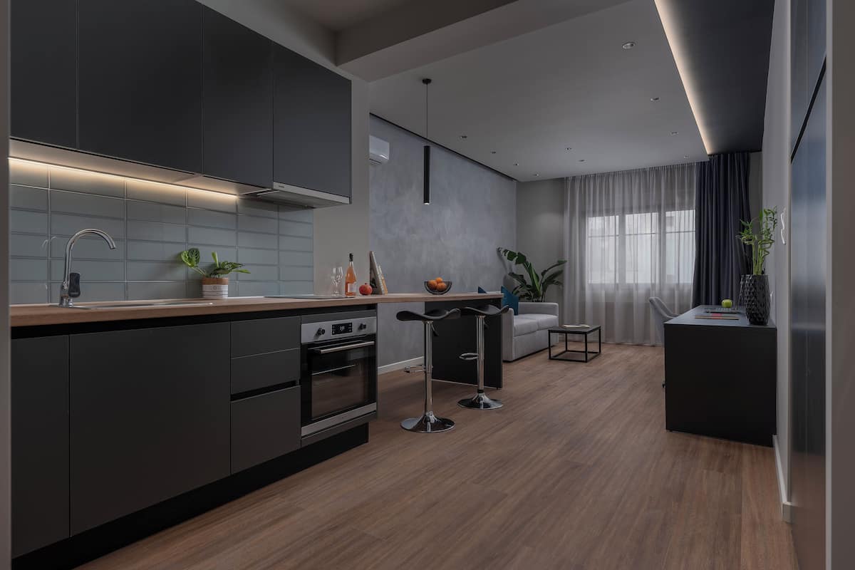 Eine moderne Küche mit dunklen Schränken, einer Holz Arbeitsplatte und einem eingebauten Backofen. Zwei Barhocker und ein kleiner Tisch mit Blumen stehen bereit.