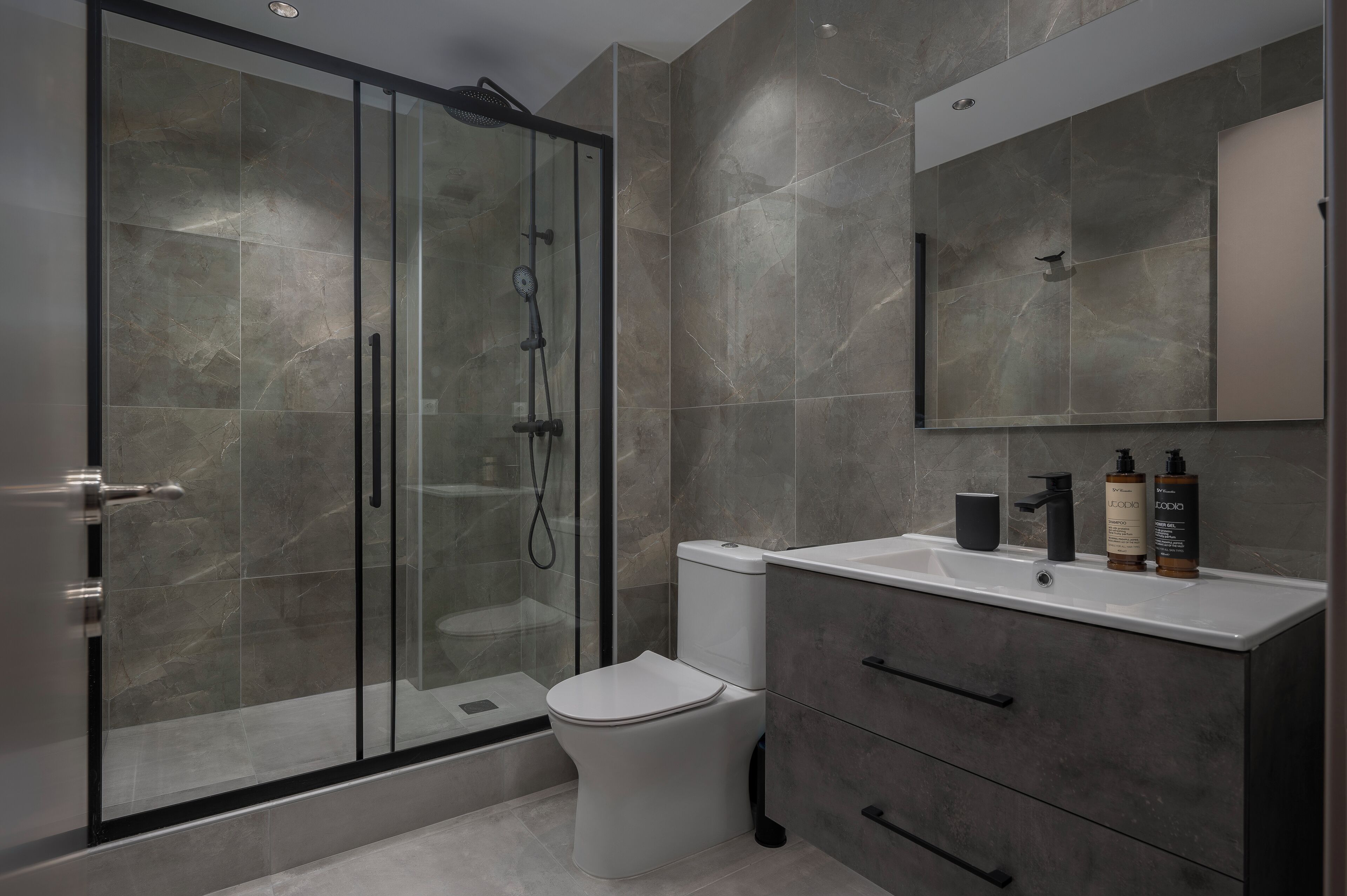 A modern bathroom with a glass-enclosed shower, a white toilet, and a vanity with a mirror and toiletries.