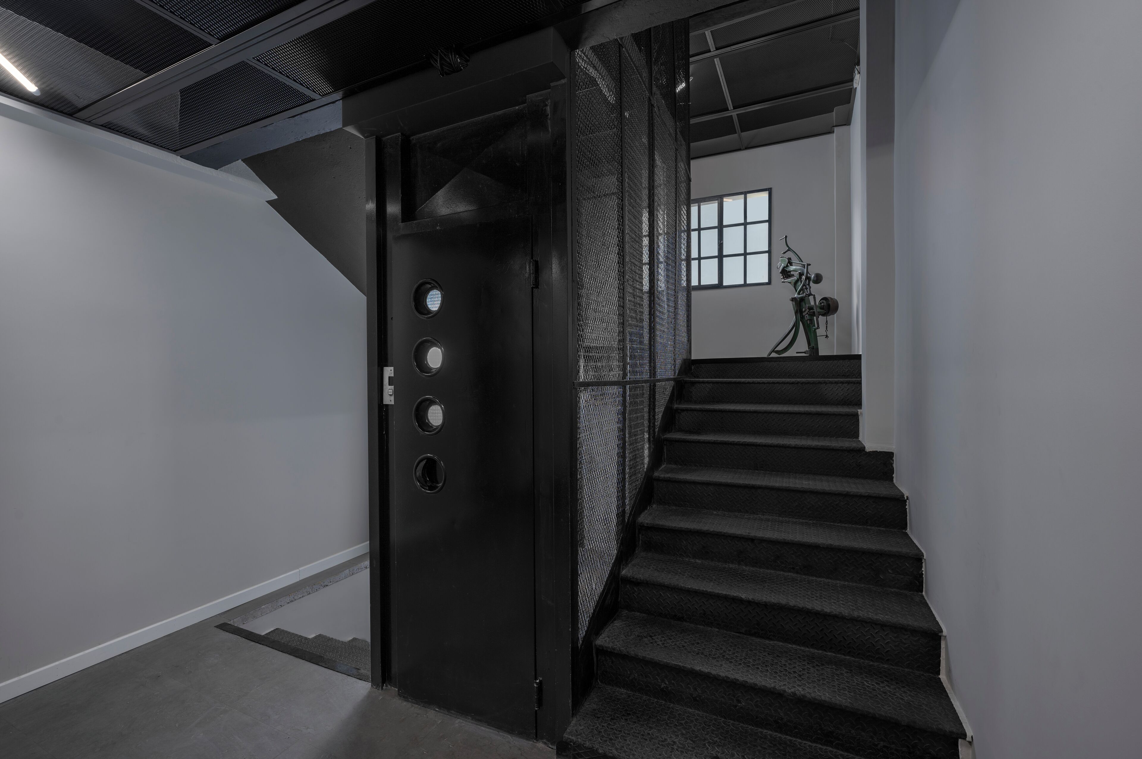 A staircase leading to a room with a metal door, a window, and a bicycle in the background.