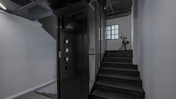 Eine Treppe führt zu einem Raum mit einer Metalttür, einem Fenster und einem Fahrrad im Hintergrund.