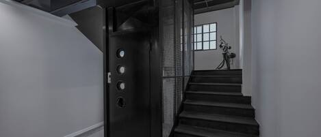 Una escalera que lleva a una habitación con una puerta de metal, una ventana y una bicicleta al fondo.