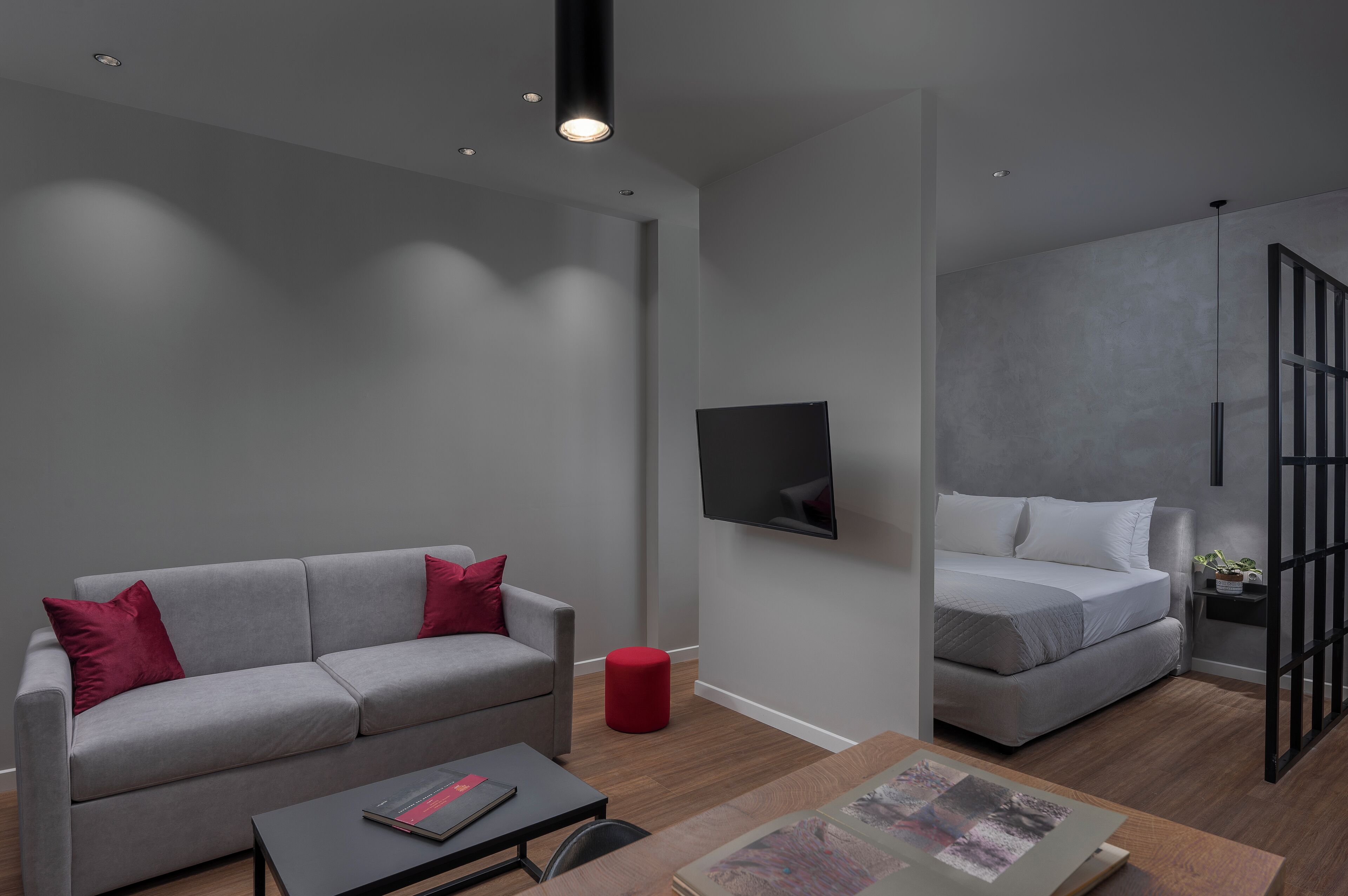 A modern living room with a grey sofa, a red ottoman, a coffee table, and a flat-screen TV mounted on the wall.