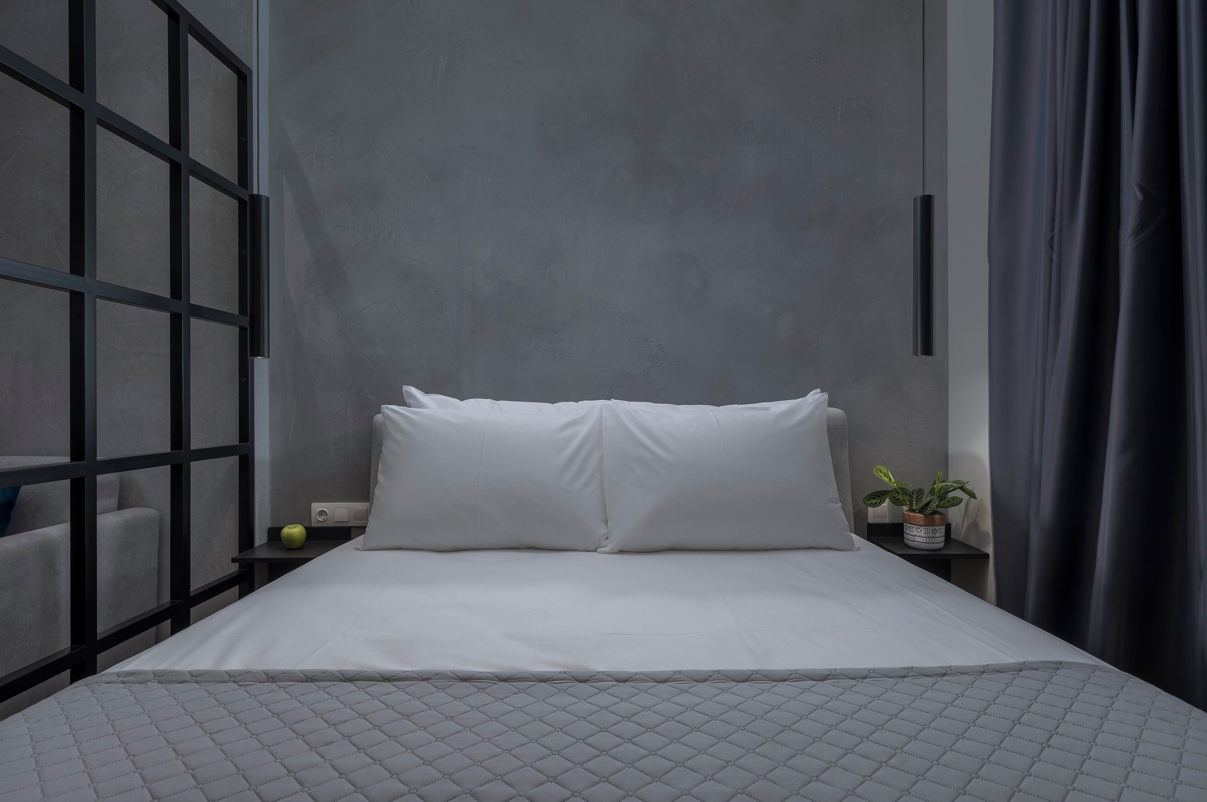 Un dormitorio moderno con una cama grande, una mesita de noche con una planta y vistas a través de una ventana con cortina.