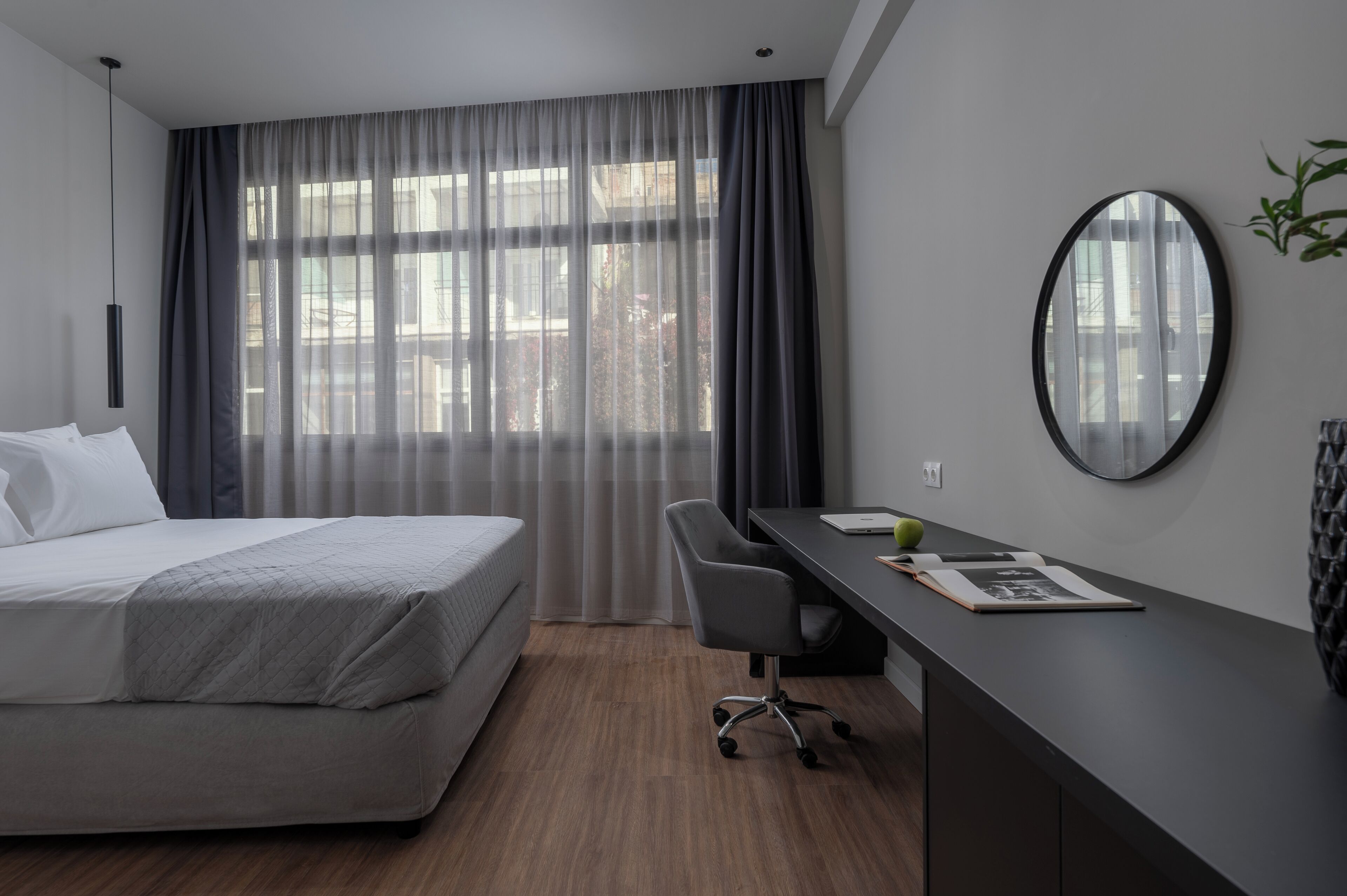 A modern hotel room with a bed, a desk, and a large window with curtains.