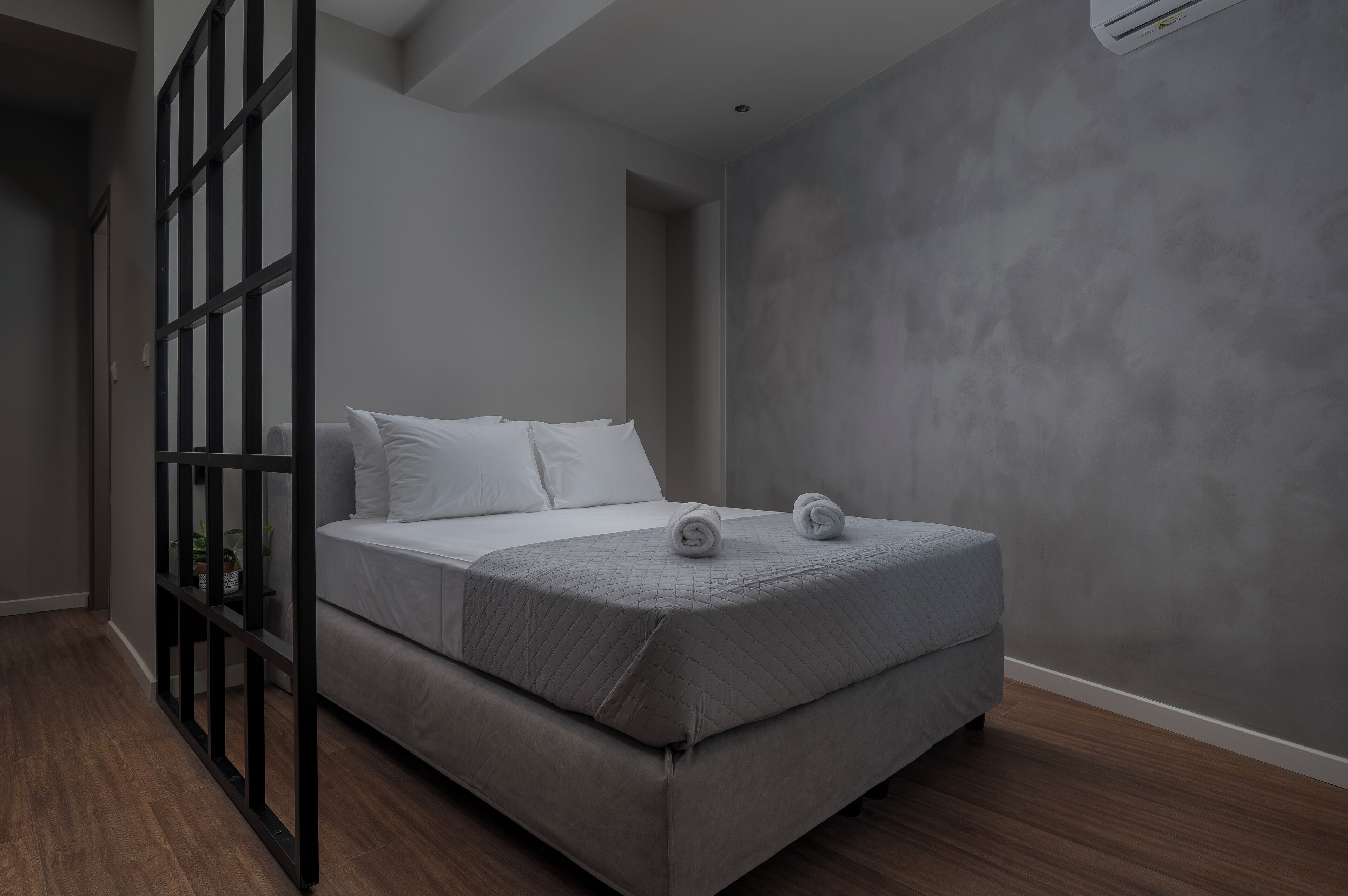A modern bedroom with a bed, a black metal partition, and a grey textured wall.