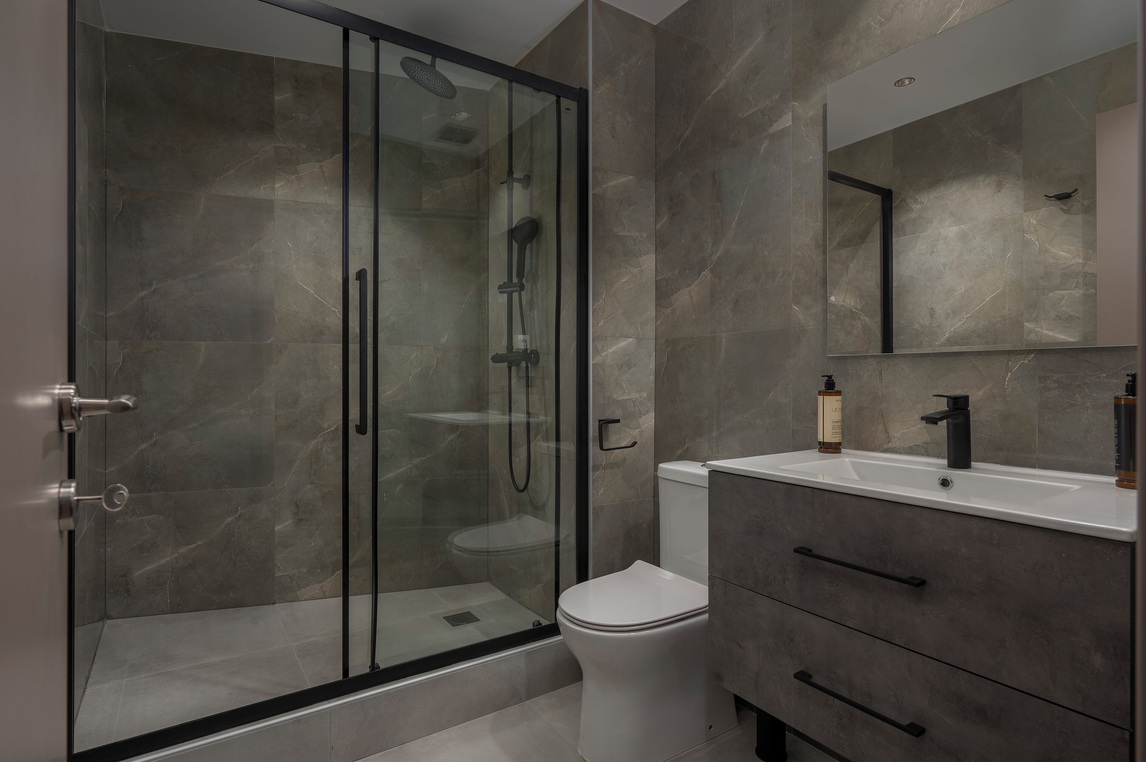 Une salle de bain moderne avec une douche à parois de verre, des toilettes blanches et un meuble-lavabo avec un miroir.