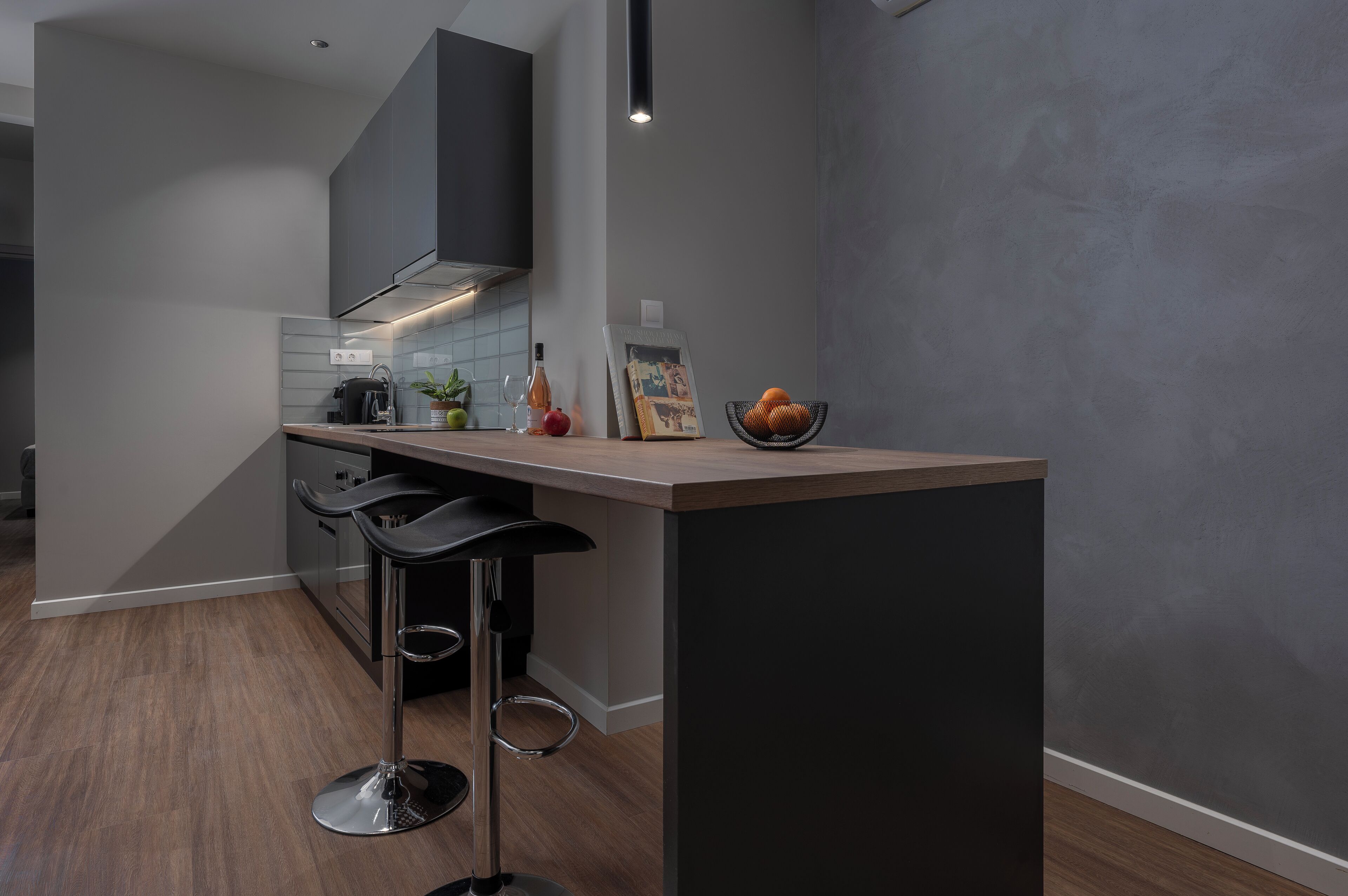A modern kitchen with a bar area, featuring a dark countertop, two bar stools, and a small island.