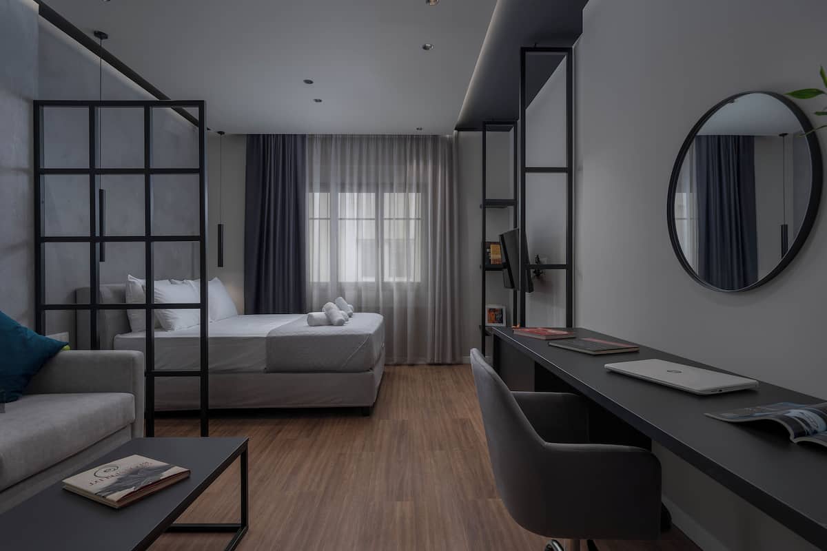 Ein modernes Hotelzimmer mit Bett, Schreibtisch, Stuhl, Sofa und einem großen Spiegel.