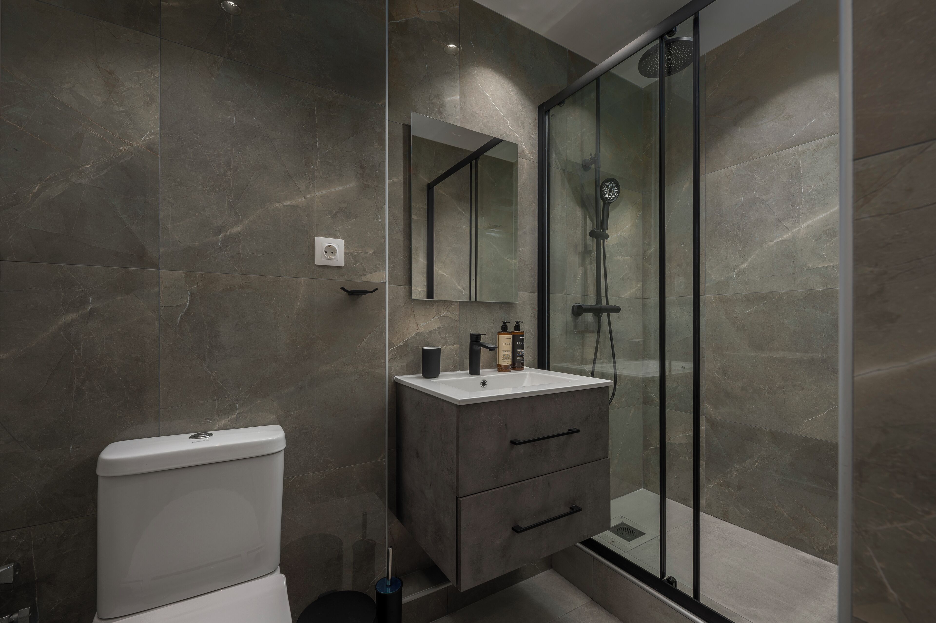 A modern bathroom with a toilet, a vanity with a mirror, and a glass-enclosed shower area.