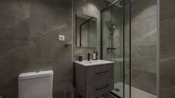 Un baño moderno con inodoro, tocador con espejo y zona de ducha con mampara de vidrio.