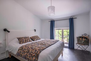 Ein Schlafzimmer mit Bett, einem Fenster mit Vorhängen, einer Pendelleuchte und einem Sessel.