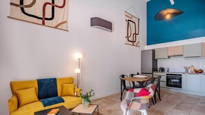 A modern living room with a yellow sofa, a dining table, and a kitchen area with cabinets and a stove.