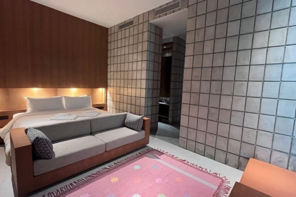 Quarto de hotel moderno com cama, sofá e parede revestida de azulejos.