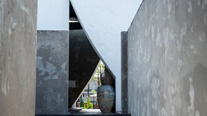 Ein schmaler Korridor mit einer großen Vase in der Mitte, umgeben von Betonwänden und einer geneigten Decke.