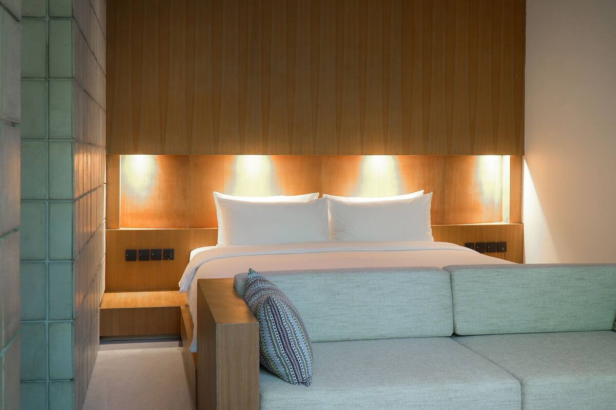 A modern hotel room with a bed, a sofa, and wall-mounted lighting.