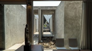 Ein modernes Interieur mit einer Steinstatue, einem Holztisch und Blick durch eine Glaswand.