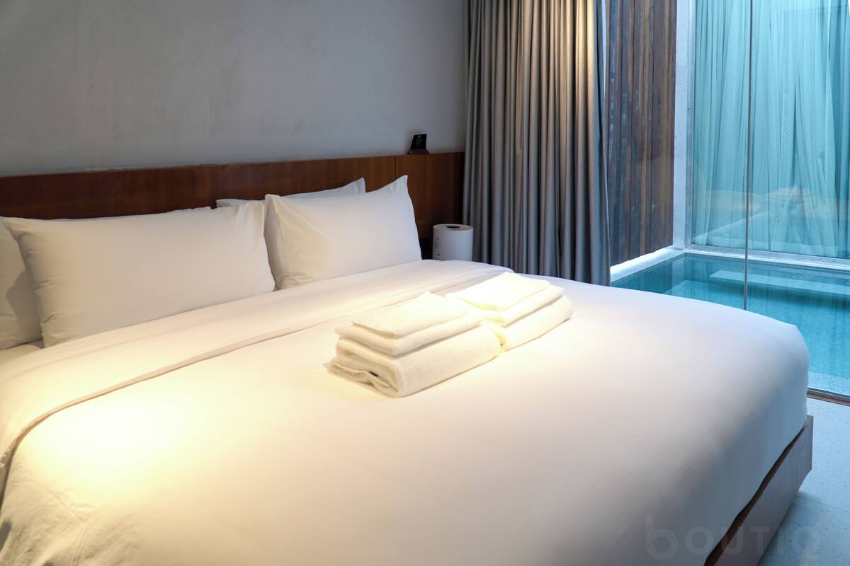 A neatly made bed with white linens and towels, a wooden headboard, and a window with curtains.