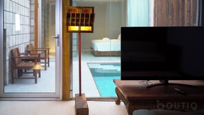 Ein Hotelzimmer mit Fernseher, Holzmöbeln, einer Glastür, die auf einen Balkon führt, und einem Bett mit weißer Bettdecke.