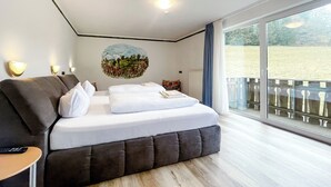 Una habitación de hotel moderna con una cama grande, vista a un campo de hierba y un balcón con barandilla.