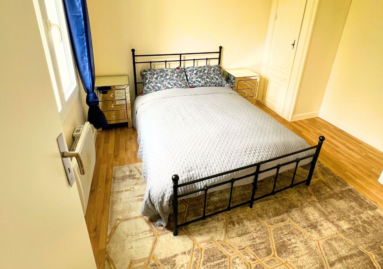Ein Schlafzimmer mit einem Metallbettgestell, einer gemusterten Bettdecke, einem Nachttisch und einem Beistelltisch.