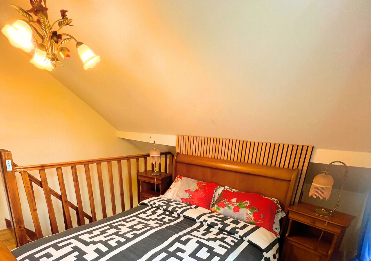 Een slaapkamer met een houten hoofdbord, een bed met een decoratieve spreideken en een nachtkastje met een lamp.