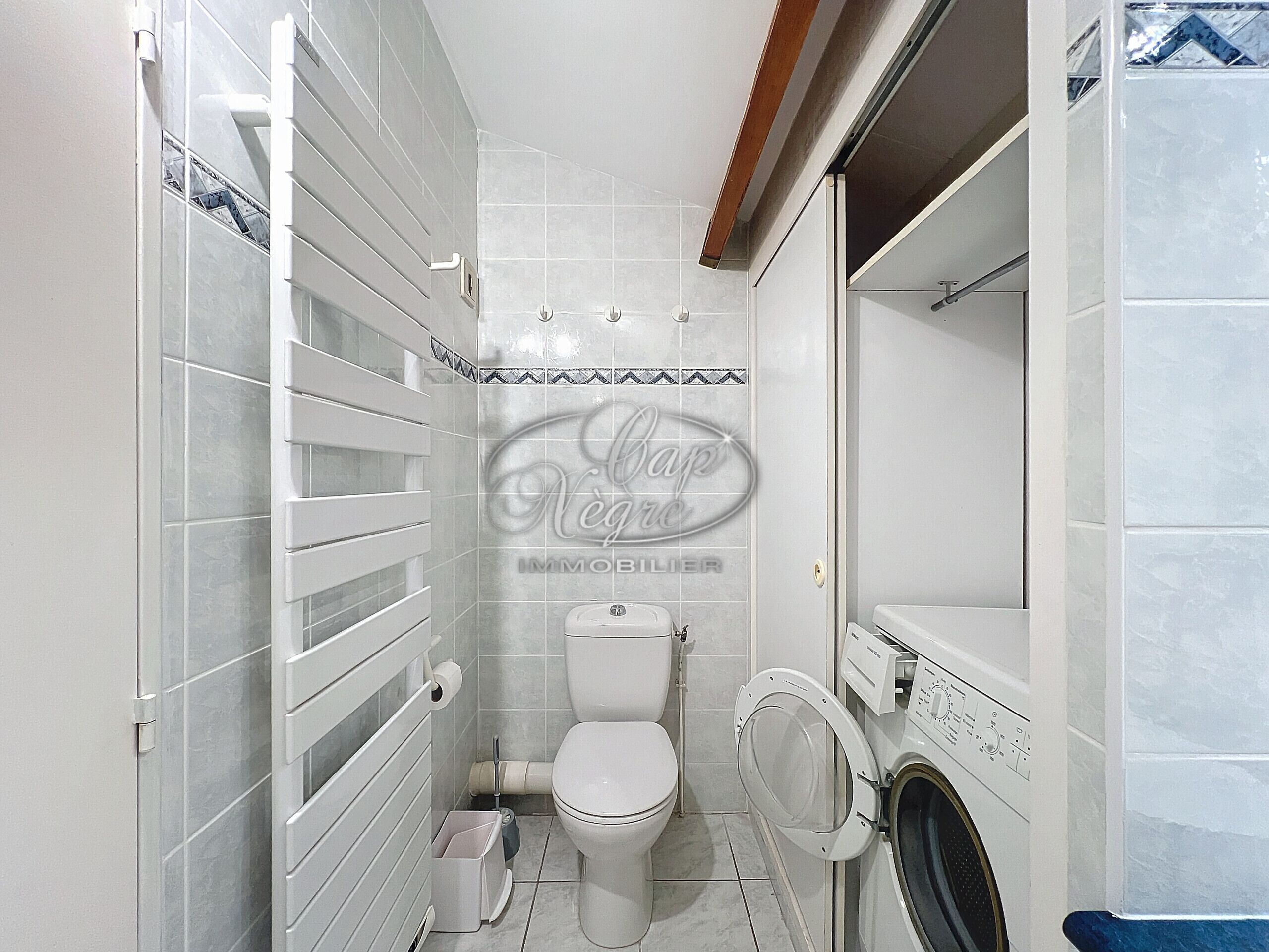 Een kleine badkamer met toilet, wasmachine en douchecabine.