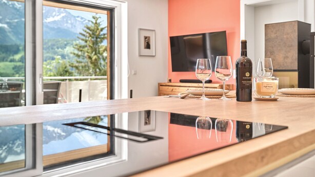 A modern kitchen with a large window, a flat-screen TV, and a wine bottle on the counter. - The Mountain Suite Top  11 - Tauplitz Residences (Tauplitz)