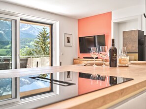 A modern kitchen with a large window, a flat-screen TV, and a wine bottle on the counter. - The Mountain Suite Top  11 - Tauplitz Residences (Tauplitz)