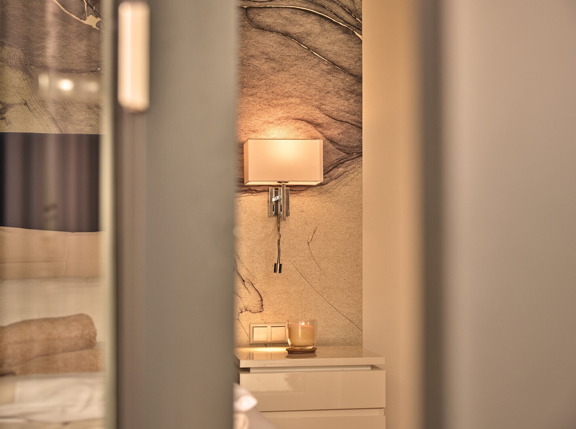 Een badkamer met een marmeren wand, een wandlamp en een klein tafeltje met een kaars.
