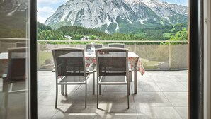 A balcony with two chairs and a table, overlooking a mountainous landscape with houses and greenery. - The Mountain Suite Top  11 - Tauplitz Residences (Tauplitz)
