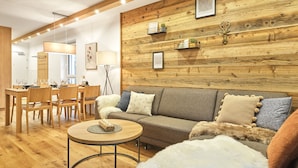 Un salon chaleureux avec un mur en bois, un canapé, une table basse ronde et un coin repas comprenant des chaises et une table.