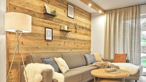 Un salon moderne avec un mur d’accent en bois, un canapé agrémenté de plusieurs coussins, une lampe sur pied et une table basse ronde.