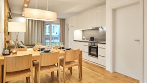Une cuisine moderne avec des armoires blanches, un four encastré et un coin repas comprenant des chaises en bois et une table dressée pour six personnes.
