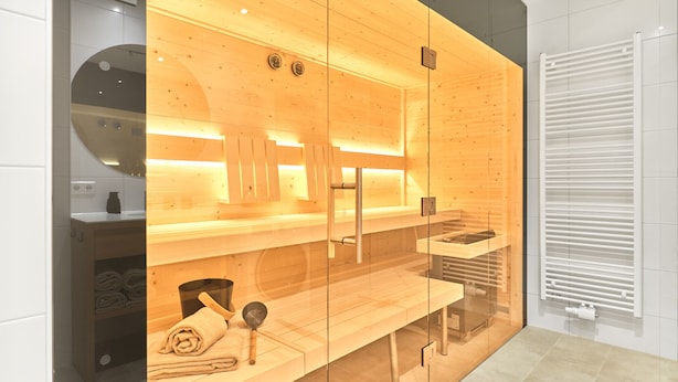 Un sauna moderne avec des murs en bois et des portes en verre, un banc et un porte-serviettes.