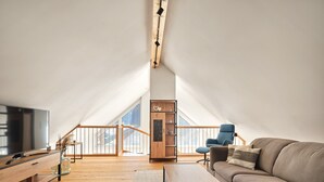 Un'ampia camera mansardata con un'ampia finestra, una scrivania in legno, un divano e una poltrona.