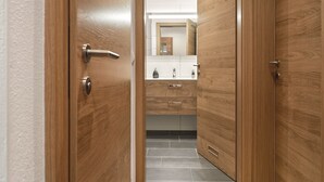 Una porta in legno che dà su un bagno con uno specchio, un lavandino e dei cassetti.