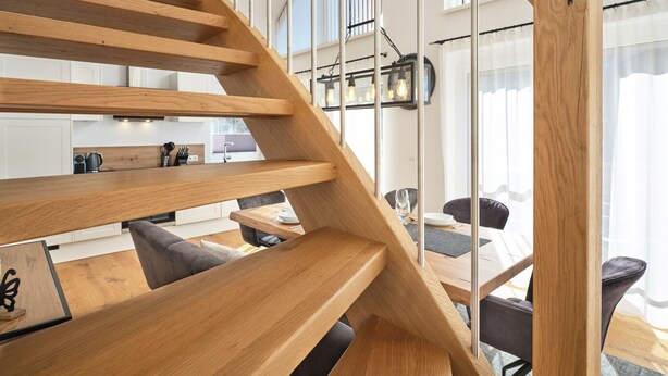 Un interno moderno con una scala a chiocciola in legno, una zona pranzo e una cucina sullo sfondo.