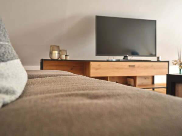 A bedroom with a bed, a wooden dresser, and a television on the wall.