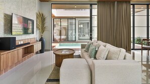 Una sala de estar moderna con una televisión de pantalla plana, un sofá, una mesa de centro y un ventanal con cortinas.