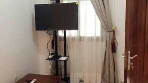 Une pièce avec un téléviseur posé sur un meuble, une petite table avec une télécommande et une porte.