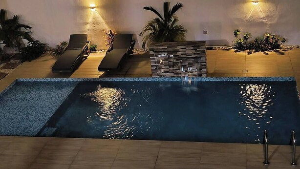 Une piscine équipée de chaises longues et de lampes fixées au mur.