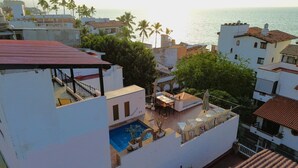 Zona de piscina en la azotea con vista al mar, rodeada de edificios y palmeras.