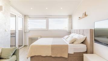 A modern bedroom with a large bed, a TV, and a balcony with a city view.