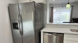 A stainless steel refrigerator with a water dispenser, a dishwasher, and a countertop with a sink.