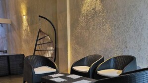 A modern lounge area with wicker furniture, a hanging chair, and a textured wall.