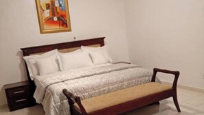 A bedroom with a bed, a nightstand, a chair, and a painting on the wall.