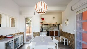 A modern kitchen with a dining area, featuring a white table, chairs, and a hanging light fixture.